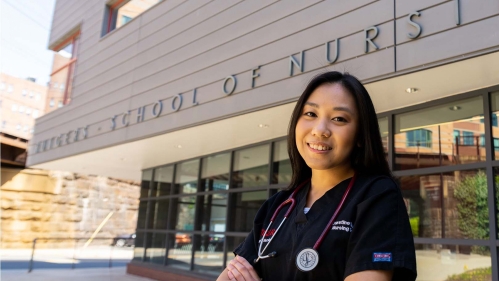 A nursing student stands in front of the School of Nursing