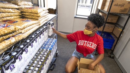 A student wearing a Rutgers T-shirt adds groceries to shelves in the Newark Food Pantry