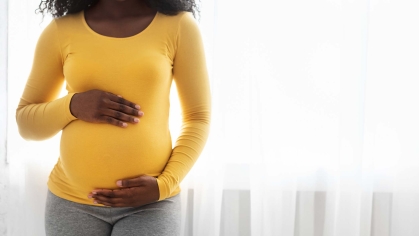 A pregnant woman wearing a yellow shirt cradles her belly