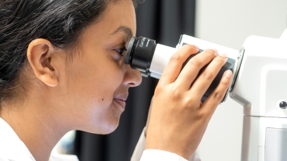 A student researcher wearing a lab coat peers into a microscope