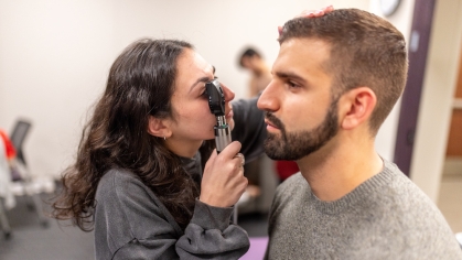 A health professions student looks into a patient's eye