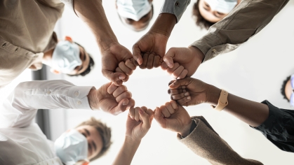Below view of young diverse group of people in protective medical masks making fist bump standing in circle.