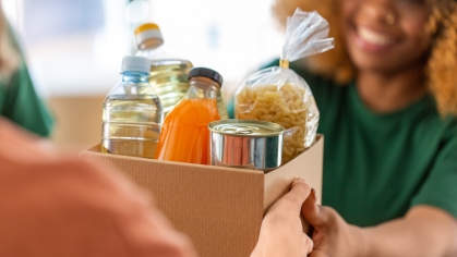 A student hands a box of food supplies to a person at a food bank