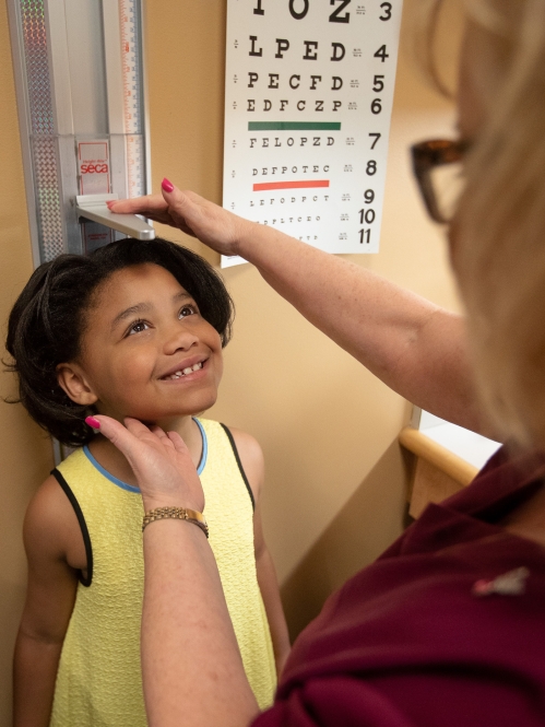 A nurse measures a child's height against a wall in an exam room