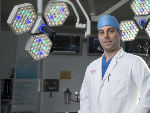 A Rutgers Health doctor wearing a white coat and blue cap stands in an operating room