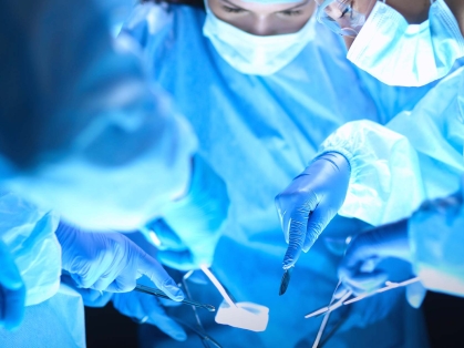 Doctors holding instruments look down at a patient in an operating room