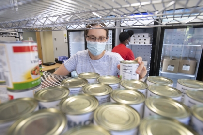 A person stocks cans on shelves at the RBHS Food Pantry
